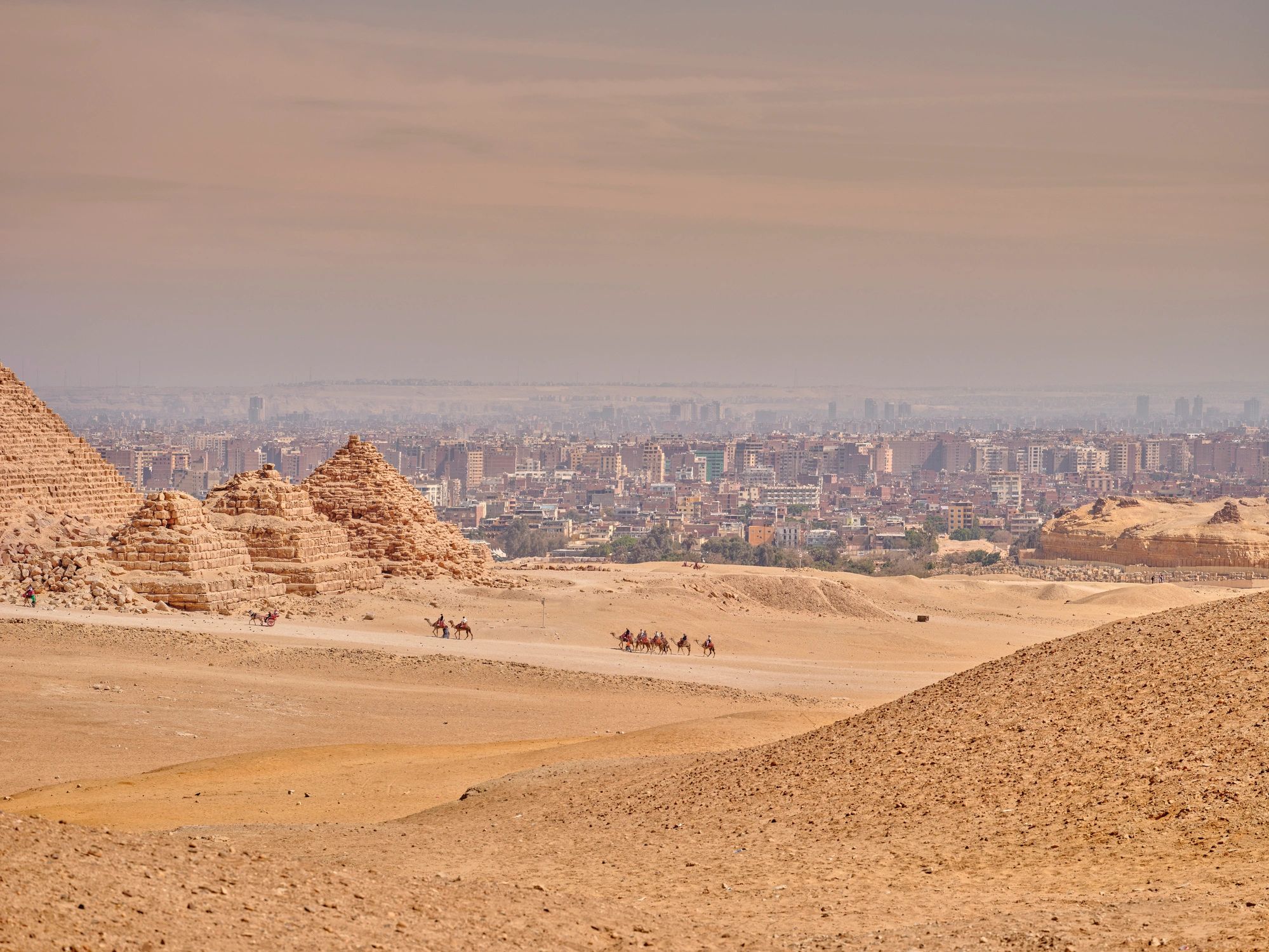 Pyramids of Giza desert view with camel caravan and Cairo skyline in Egypt at dusk
